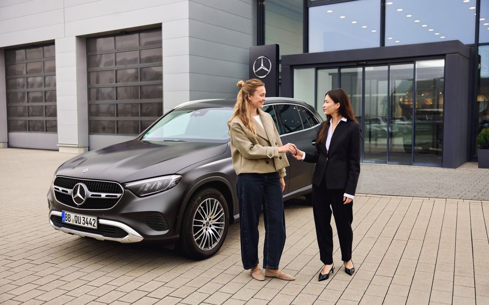Customer receiving the key to a Mercedes-Benz GLC SUV outside a dealership